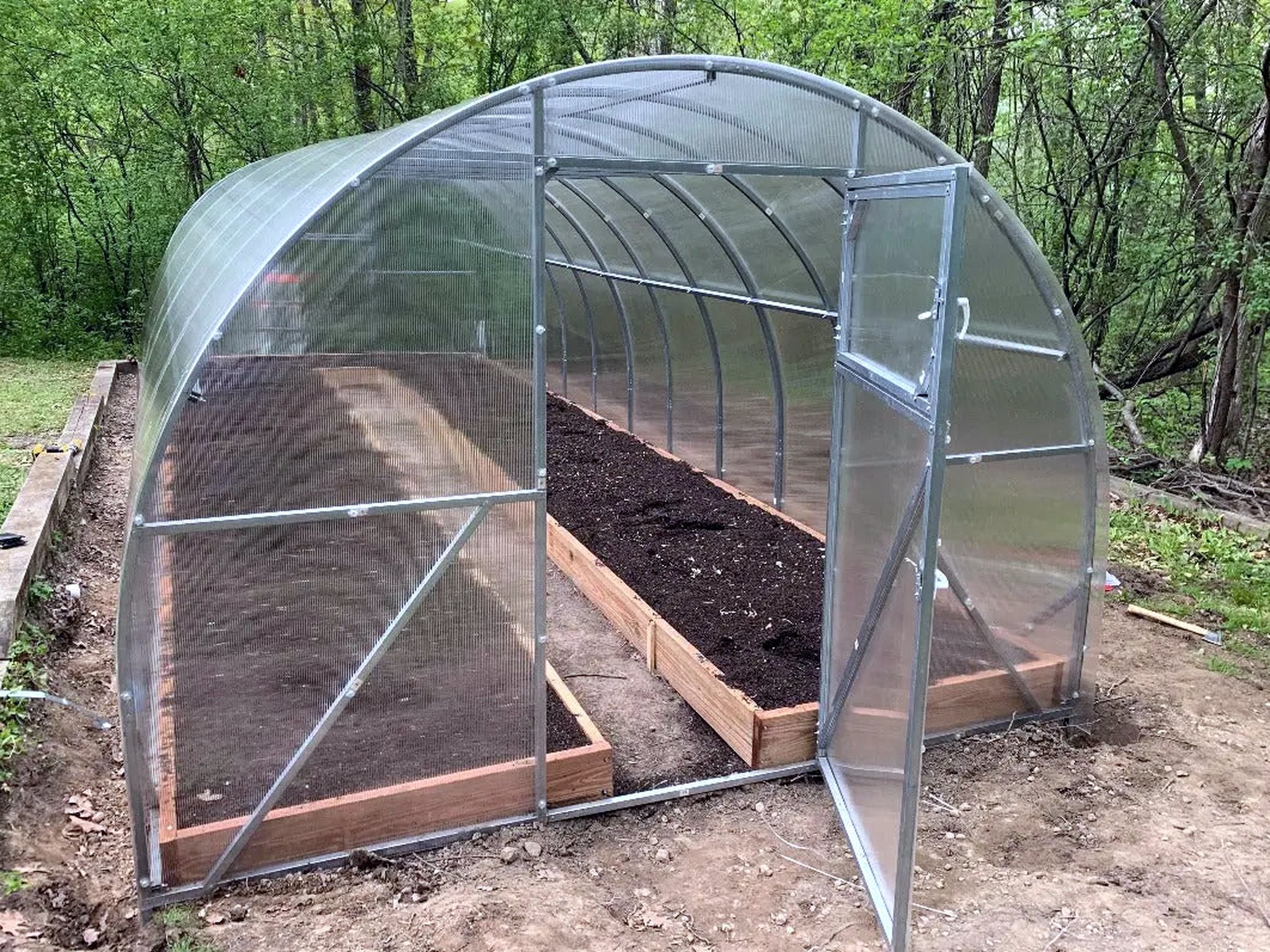 The inside of an Arc Series greenhouse, showing the galvanized steel hoops, cross bracing and a raised bed