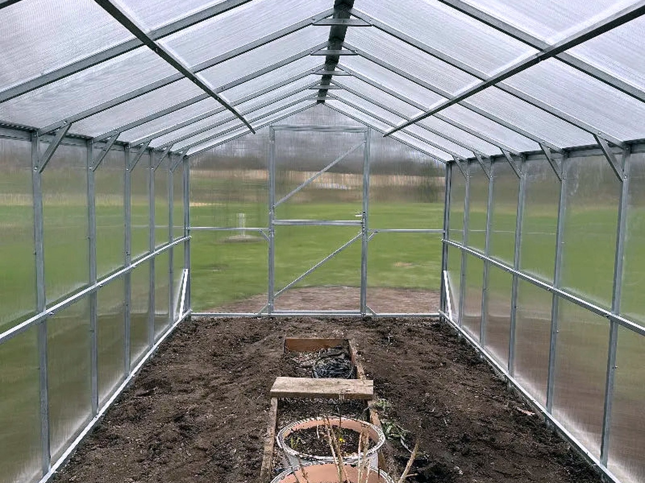 Inside a Gable Series greenhouse: light diffused through twinwall panels onto a galvanized steel frame and prepared beds.