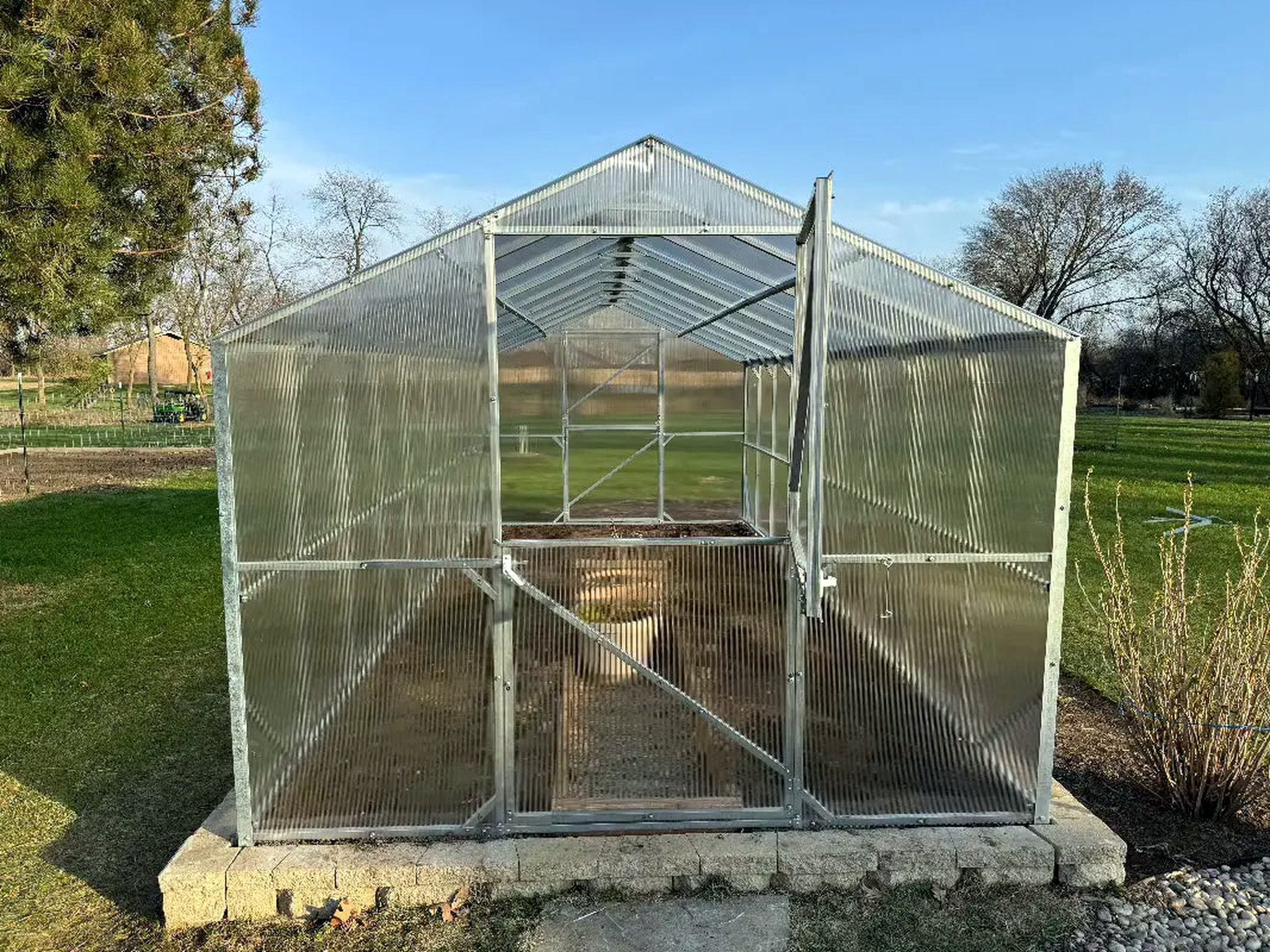 Gable Series greenhouse seen head on with its Dutch door open under a pitched twinwall roof