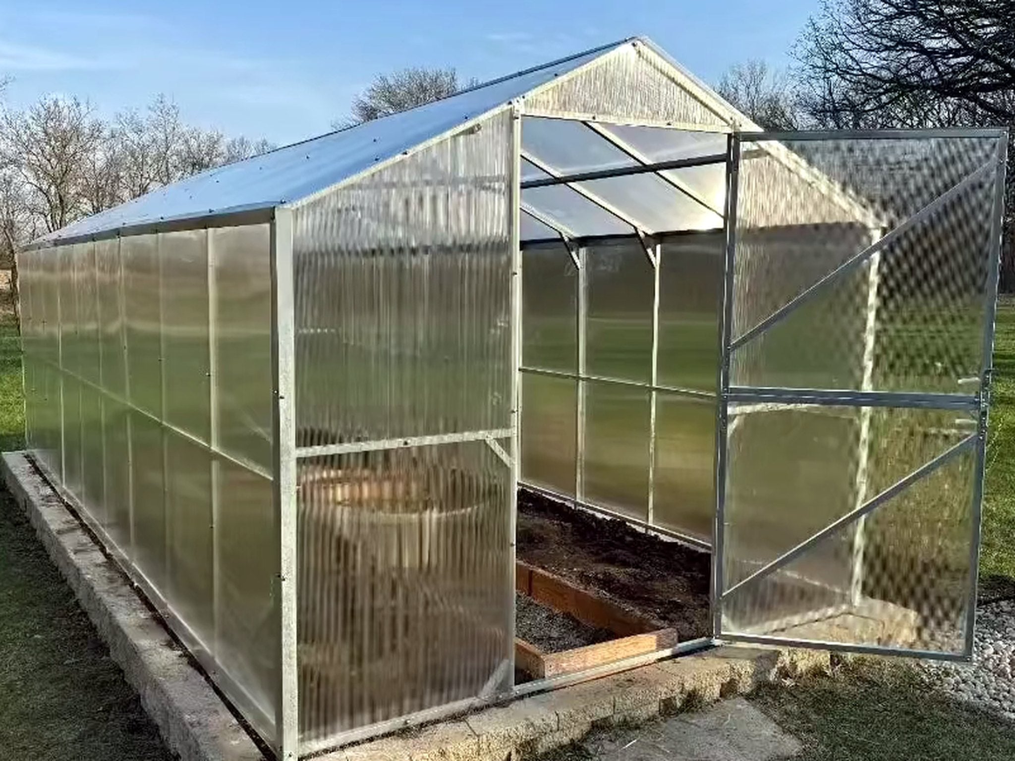 Gable Series greenhouse with straight walls and a pitched roof, its Dutch door standing open