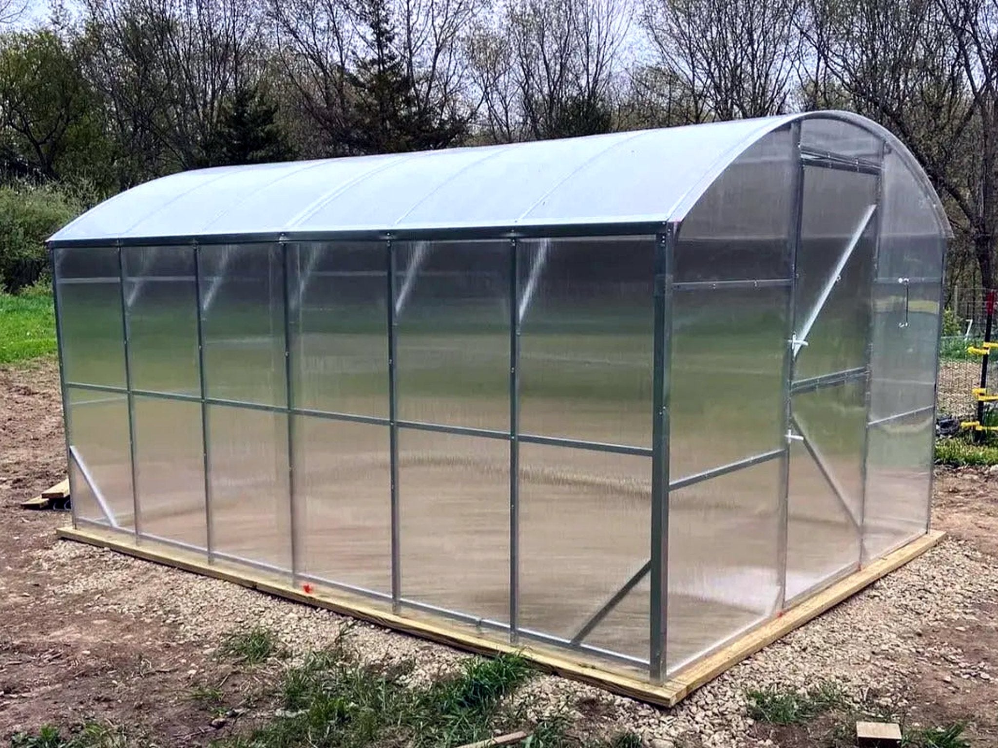 A Loft Series greenhouse with straight walls and an arched roof, sitting on a timber base on prepared ground